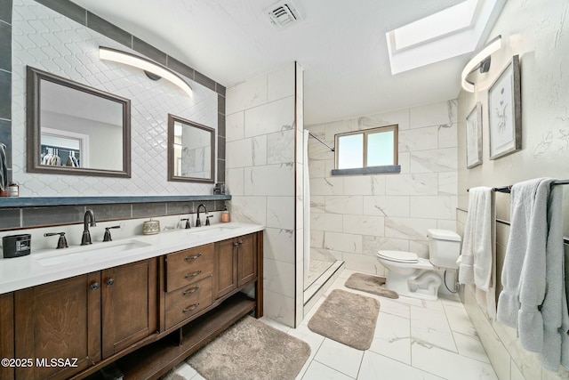 bathroom with a tile shower, a skylight, tile walls, vanity, and toilet