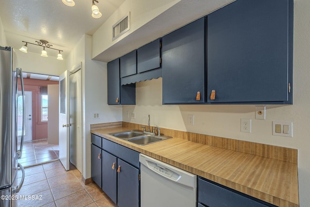 kitchen featuring blue cabinetry, sink, light tile patterned floors, stainless steel refrigerator, and dishwasher