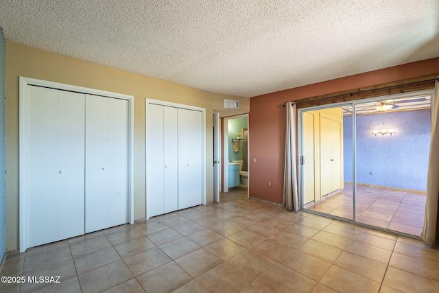 unfurnished bedroom featuring ensuite bathroom, two closets, a textured ceiling, and light tile patterned floors