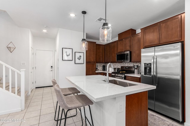 kitchen with hanging light fixtures, stainless steel appliances, tasteful backsplash, an island with sink, and light tile patterned flooring