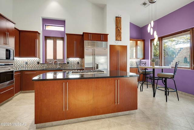 kitchen with visible vents, dark countertops, a center island, built in appliances, and a sink