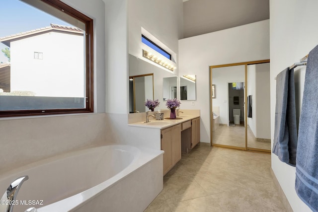 full bath with a healthy amount of sunlight, a high ceiling, a bath, and vanity