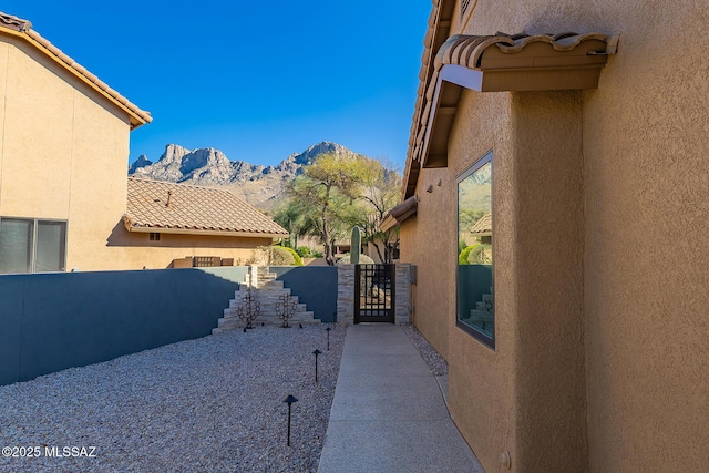 view of side of home featuring stucco siding, a gate, a mountain view, fence, and a tiled roof