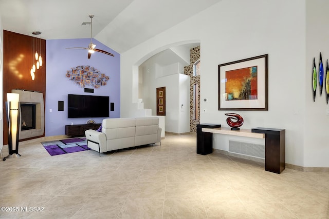 living room featuring high vaulted ceiling, a tiled fireplace, arched walkways, and a ceiling fan