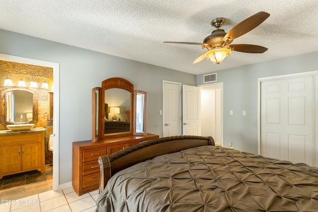 tiled bedroom featuring ceiling fan, ensuite bathroom, and a textured ceiling