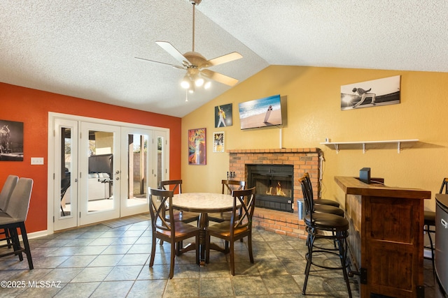 dining room with french doors, lofted ceiling, a textured ceiling, ceiling fan, and a fireplace