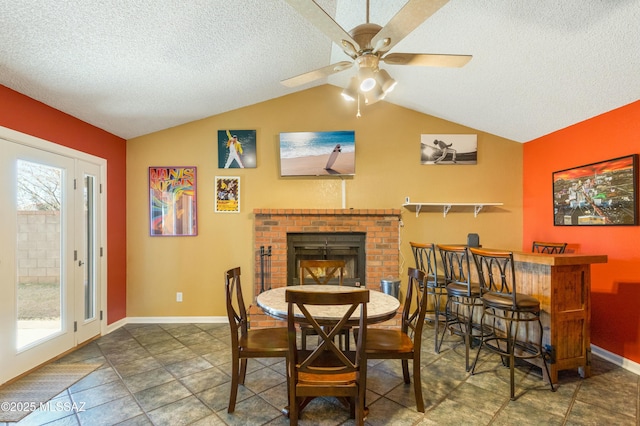 dining area featuring lofted ceiling, ceiling fan, a fireplace, and a textured ceiling