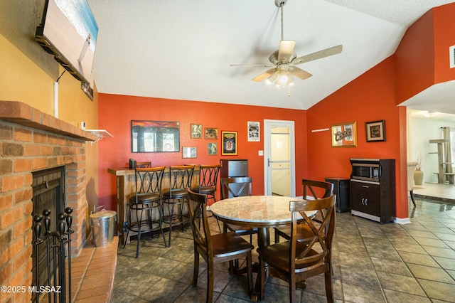 tiled dining room with vaulted ceiling, a fireplace, and ceiling fan