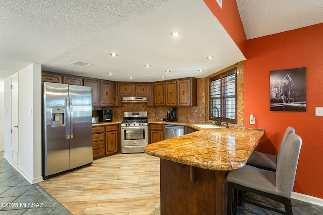 kitchen with sink, a kitchen breakfast bar, kitchen peninsula, stainless steel appliances, and decorative backsplash