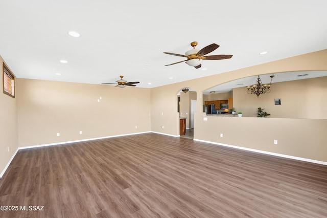 unfurnished living room featuring ceiling fan with notable chandelier and dark hardwood / wood-style flooring