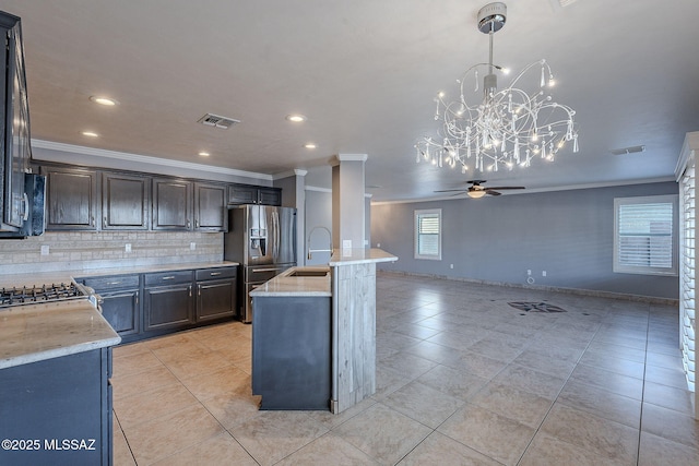 kitchen with sink, hanging light fixtures, stainless steel fridge, an island with sink, and light stone countertops