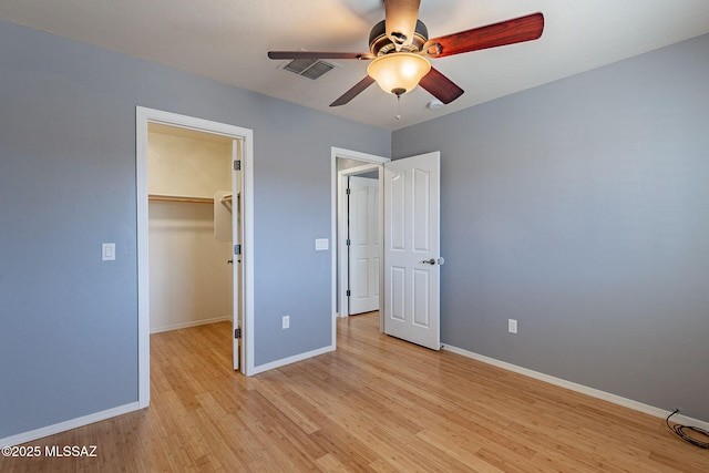 unfurnished bedroom featuring ceiling fan, a walk in closet, light hardwood / wood-style floors, and a closet