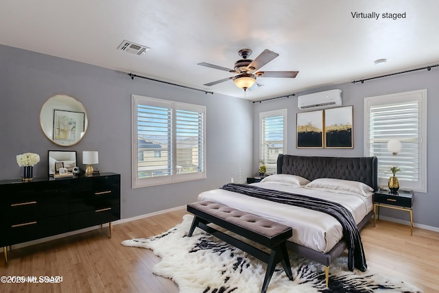 bedroom with ceiling fan, a wall mounted AC, and light hardwood / wood-style flooring