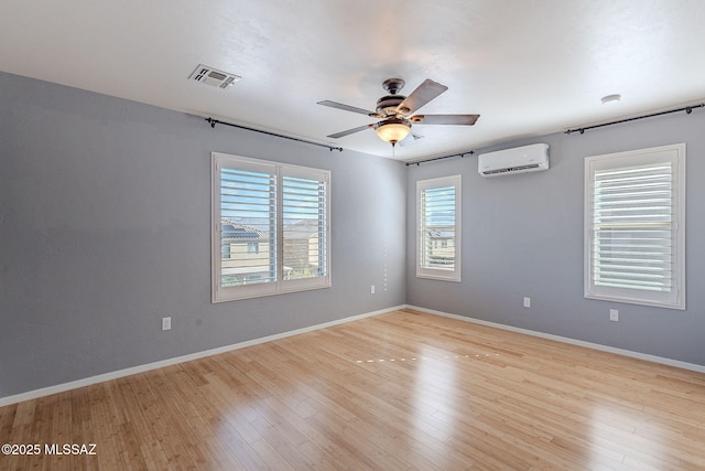 spare room with a wall mounted AC, ceiling fan, and light hardwood / wood-style flooring