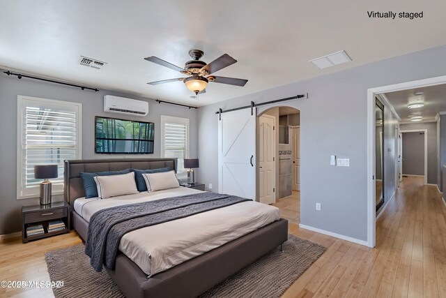 bedroom with ceiling fan, a barn door, a wall mounted air conditioner, and light hardwood / wood-style floors