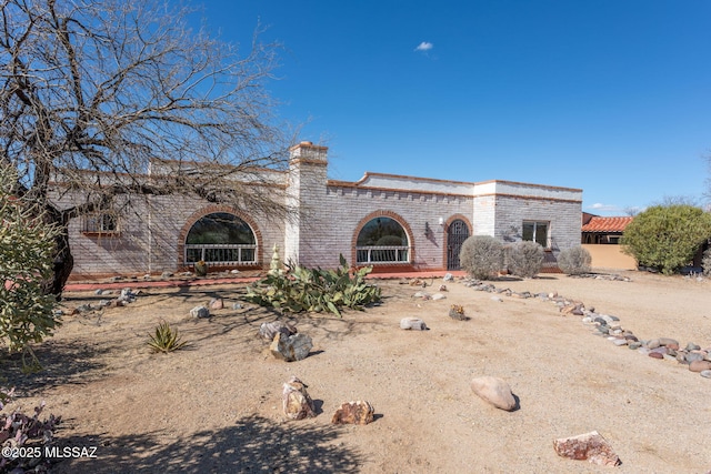 view of front of house featuring brick siding, driveway, and a chimney