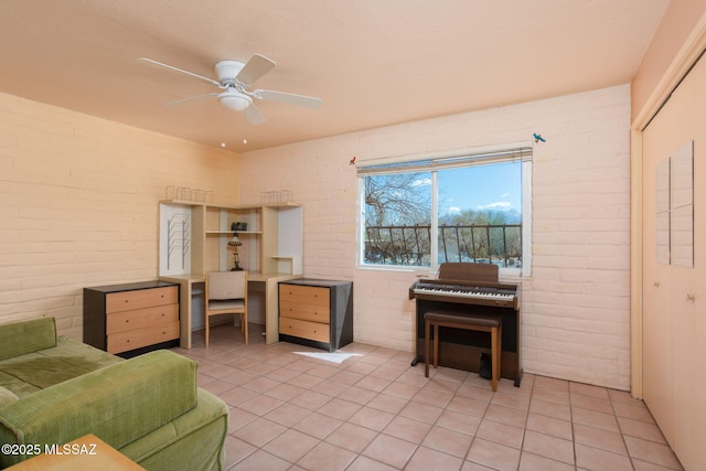 living area with a ceiling fan, light tile patterned flooring, and brick wall