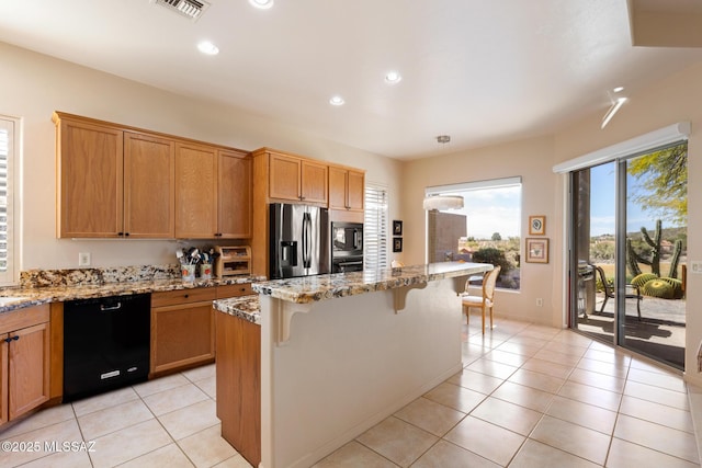 kitchen with light tile patterned flooring, visible vents, a kitchen breakfast bar, light stone countertops, and black appliances