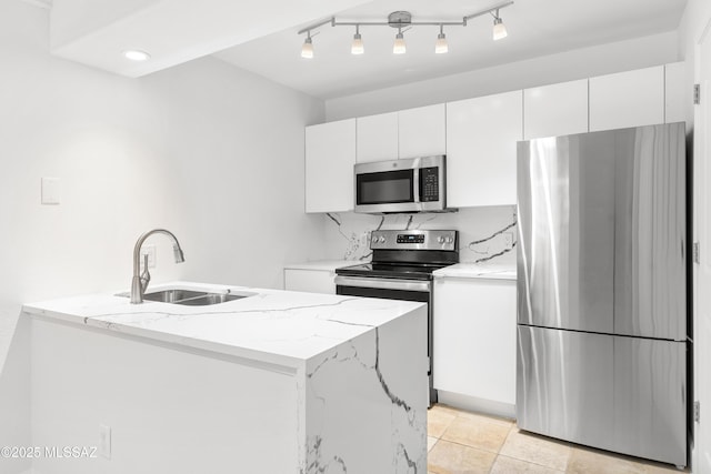 kitchen with sink, a kitchen island with sink, stainless steel appliances, light stone countertops, and white cabinets