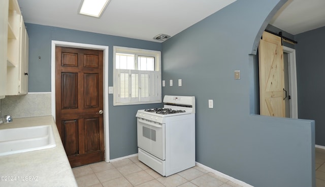 kitchen featuring sink, light tile patterned floors, gas range gas stove, and a barn door