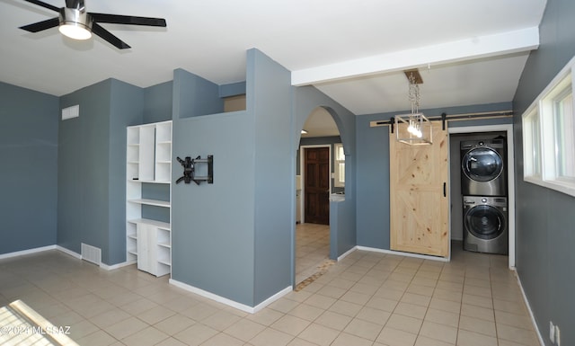 interior space featuring lofted ceiling, stacked washer and dryer, light tile patterned floors, ceiling fan, and a barn door