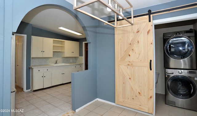 laundry room with stacked washing maching and dryer, a barn door, sink, and light tile patterned flooring