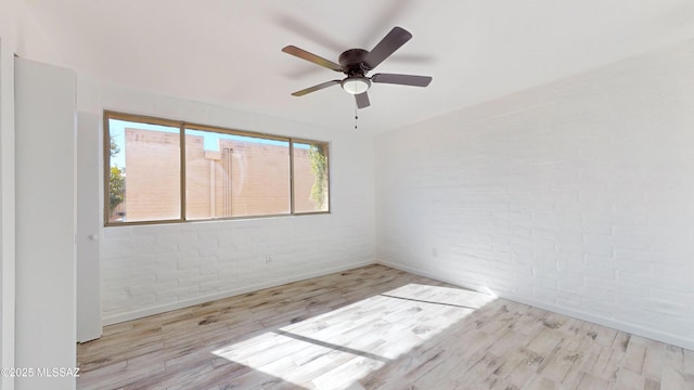 unfurnished room featuring ceiling fan, brick wall, and light hardwood / wood-style floors