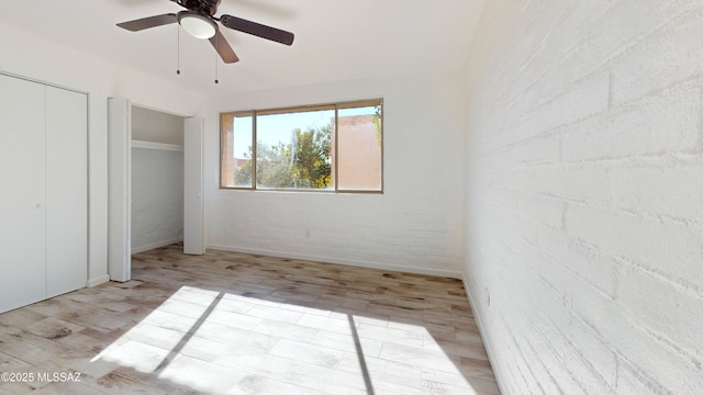 unfurnished bedroom with ceiling fan, brick wall, and light wood-type flooring