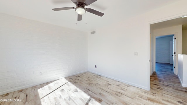 unfurnished room featuring light hardwood / wood-style floors, ceiling fan, and brick wall