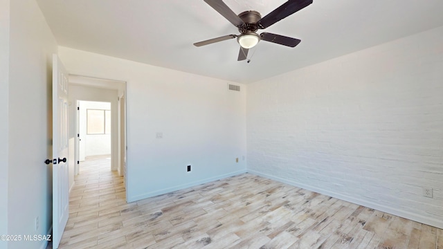 spare room with ceiling fan, brick wall, and light wood-type flooring