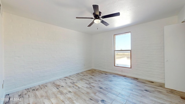 empty room with ceiling fan, brick wall, and light hardwood / wood-style floors