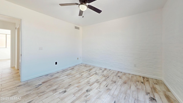 empty room featuring ceiling fan, brick wall, and light hardwood / wood-style floors