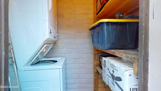 washroom featuring brick wall and stacked washer / drying machine