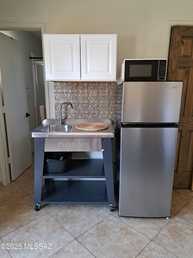 kitchen featuring light tile patterned flooring, stainless steel refrigerator, built in microwave, white cabinetry, and tasteful backsplash