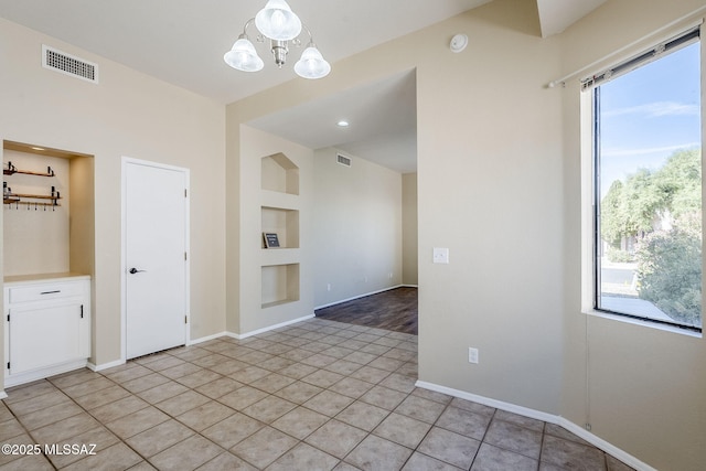 tiled empty room featuring an inviting chandelier and built in features