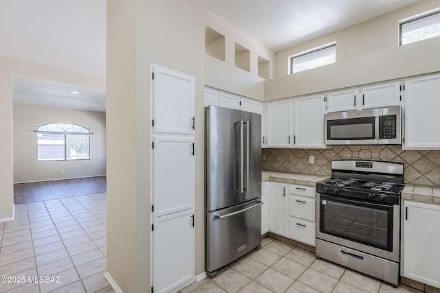 kitchen featuring stainless steel appliances, tile counters, white cabinets, and decorative backsplash