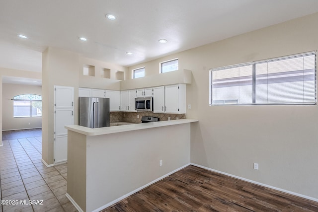 kitchen featuring hardwood / wood-style flooring, appliances with stainless steel finishes, white cabinetry, backsplash, and kitchen peninsula