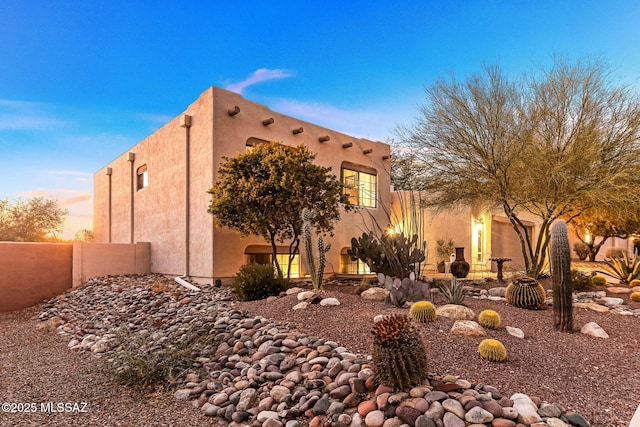 property exterior at dusk with stucco siding, a garage, and fence