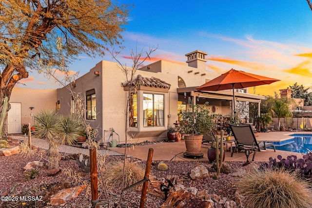 back house at dusk featuring a fenced in pool and a patio