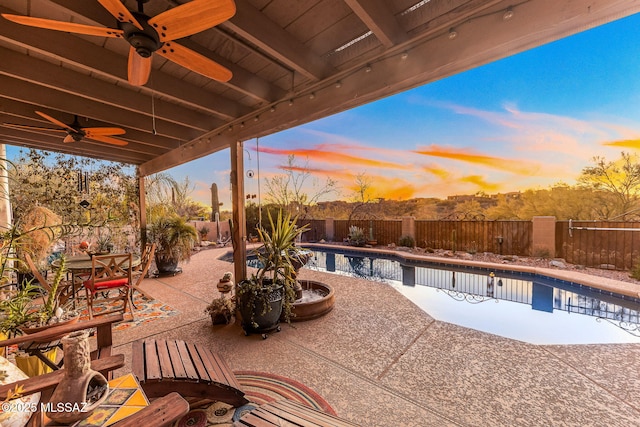 patio terrace at dusk featuring a fenced in pool and ceiling fan