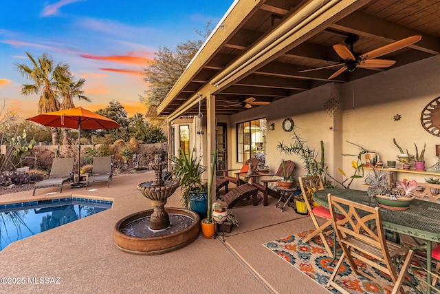 pool at dusk with a patio area and ceiling fan