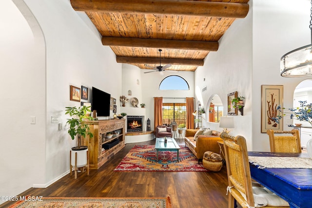 living room featuring dark hardwood / wood-style flooring, a high ceiling, ceiling fan, wooden ceiling, and beam ceiling