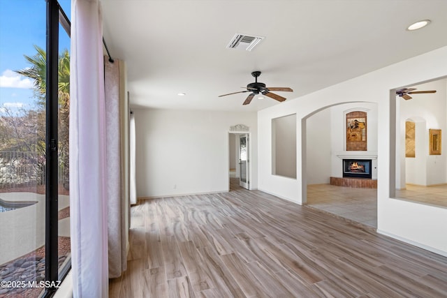 unfurnished room featuring a brick fireplace, light hardwood / wood-style floors, and ceiling fan