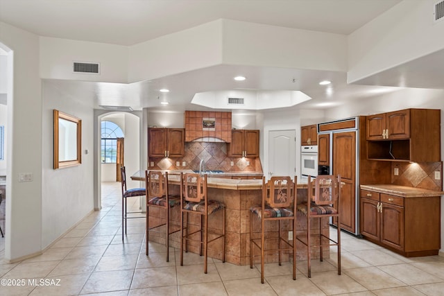 kitchen with a kitchen breakfast bar, custom range hood, a kitchen island, oven, and decorative backsplash