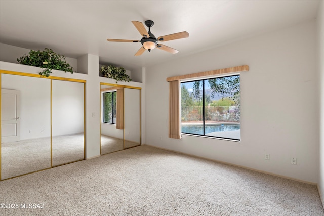 unfurnished bedroom with two closets, ceiling fan, and carpet