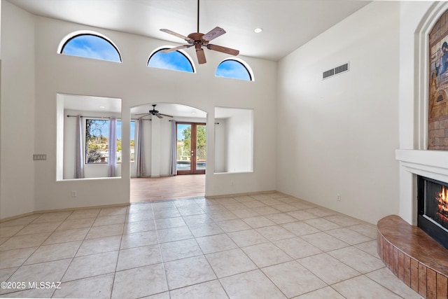 unfurnished living room with a high ceiling, light tile patterned floors, ceiling fan, and french doors