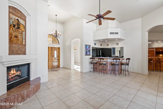 living room with ceiling fan with notable chandelier, a large fireplace, light tile patterned floors, and a towering ceiling