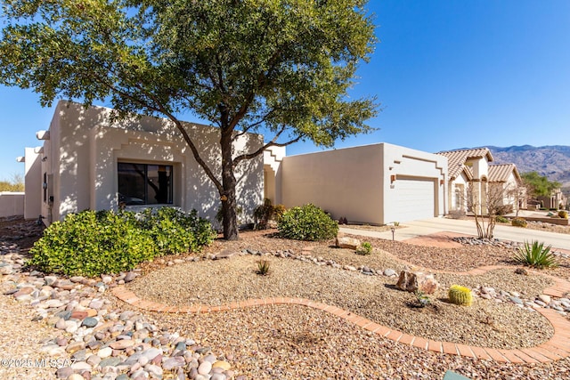 pueblo revival-style home with a mountain view, driveway, an attached garage, and stucco siding