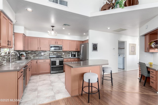 kitchen with washer / dryer, dark countertops, a center island, stainless steel appliances, and a kitchen bar