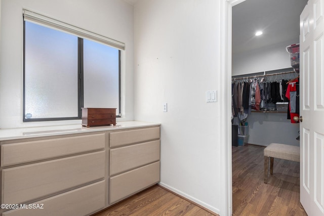 full bathroom with double vanity, a spacious closet, wood finished floors, and baseboards